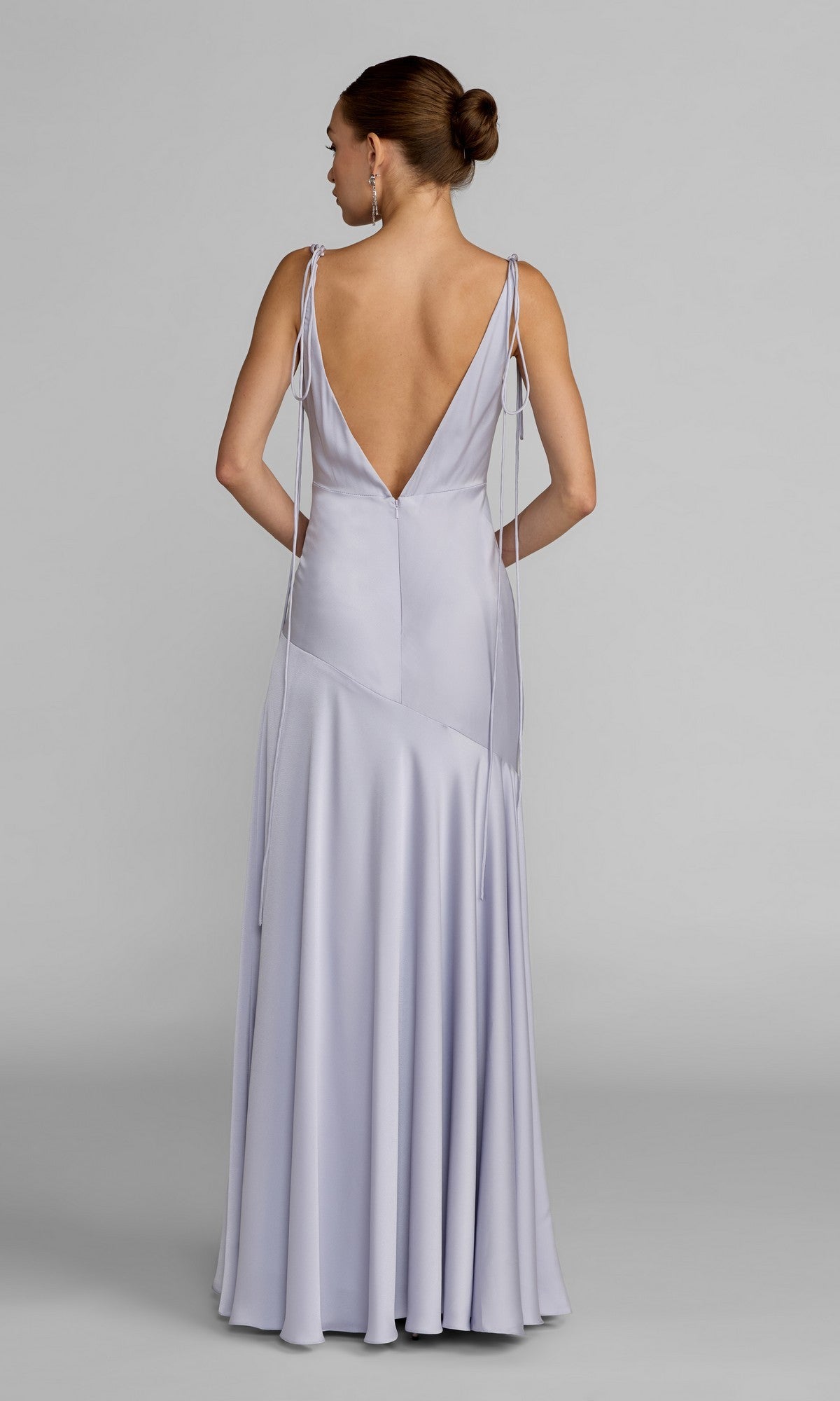 A woman poses facing away against a plain gray background, showcasing the Mac Duggal 49914 Long Formal Dress—a light purple sleeveless gown featuring an elegant A-line silhouette and a deep V-back accented with tie details.